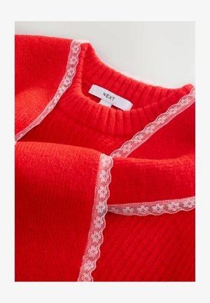 Punainen neulepaita pyöreällä kaula-aukolla, jossa on valkoista pitsiä reunoilla. Tagi lukee "NEXT." Pehmeä rakenne ja lämmin ilme.