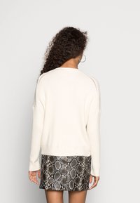 Cremfarbener gerippter Pullover mit überschnittenen Schultern, kombiniert mit einem schwarz-grauen Minirock im Schlangenmuster, der eine glatte Textur und eine taillierte Silhouette aufweist.