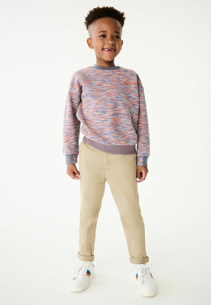Sudadera de punto multicolor con puños grises, combinada con pantalones beige y zapatillas blancas con rayas multicolores.