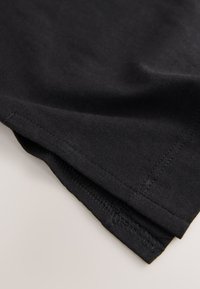 Primo piano di tessuto nero con cuciture visibili lungo i bordi dell'orlo piegato su uno sfondo chiaro.