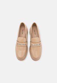 Mocassins en cuir beige à finition lisse, avec une bande argentée sur le cou-de-pied et des détails de couture autour du pourtour.