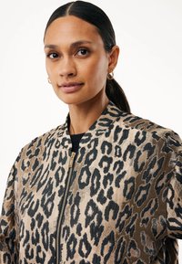 Bunda typu bomber s leopardím potiskem. Disponuje béžovým základem s černými skvrnami, zlatým zipem a žebrovaným límcem. Měkká textura, volný střih.