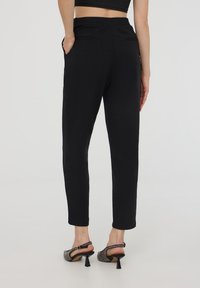 Pantaloni neri a sigaretta con fascia elasticizzata in vita, dotati di tasche laterali e una texture liscia. Abbinati a tacchi slingback texturizzati.