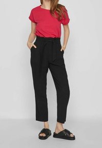 Červené tričko s krátkým rukávem doplněné o černé kalhoty s vysokým pasem, které mají zavazovací pásek, boční kapsy a černé sandály na klínku.