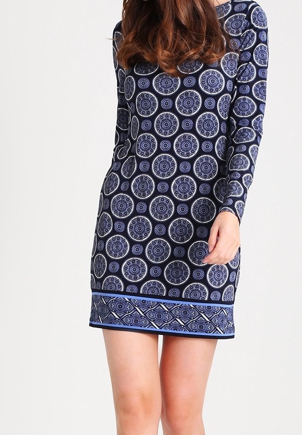 Femme portant une robe bleu marine à manches longues avec des motifs circulaires et géométriques en blanc et bleu clair.