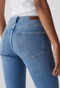 Jeans ajustados de denim azul claro. Presenta cinco bolsillos, un parche de cuero marrón en la cintura y costuras en tono a lo largo del tejido.