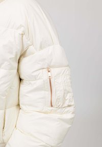 Pufferjack in off-white, met gekwiltte secties, een met rits afgesloten zak op de mouw en rosegouden hardware-accenten.