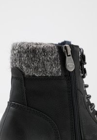 Bottine noire à la cheville avec bord-côte gris, zip métallique et devant à lacets sur fond blanc uni.