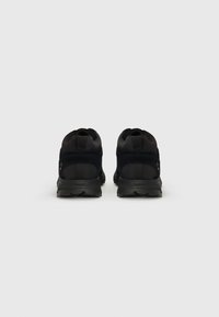 Schwarze Sportschuhe mit einem strukturierten Mesh-Obermaterial, gepolstertem Kragen und Gummilaufsohle. Verfügt über zwei Ösen und verstärkten Fersensupport.