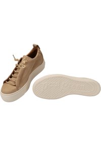 Baskets en cuir beige avec une texture lisse, dotées d'un laçage, œillets dorés et une semelle en caoutchouc blanc avec un motif en relief.