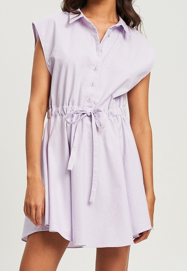 Robe chemise sans manches lilas avec un devant à boutons, taille élastique et détail à nouer. Fabriquée en tissu léger, elle présente une coupe décontractée et une jupe évasée.