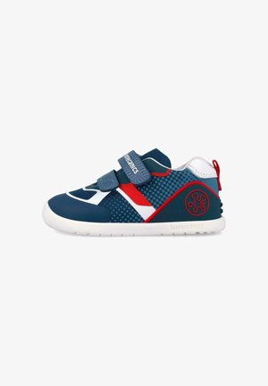 Zapatilla infantil azul y roja con suela blanca, dos tiras ajustables de Velcro, tejido de malla y una lengüeta roja en el talón.