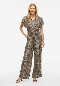 Combinaison à imprimé léopard dans des teintes beiges et brunes, manches courtes, taille ceinturée, design à jambes larges et texture de tissu lisse.