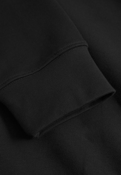 Gros plan sur le tissu d'un sweat-shirt noir montrant un poignet côtelé et une texture lisse, avec des détails de couture visibles et un col légèrement étiré.