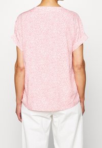 Blusa rosa a maniche corte con un sottile motivo a pois bianchi. Il tessuto è leggero, con una vestibilità morbida e scollatura rotonda.