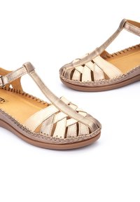 Gouden en bronzen dames sandalen met geweven bandjes, open tenen en een zachte voering. Kenmerken zijn gestikte accenten en een duurzame rubberen zool.