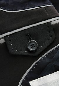 Schwarzer Stoff mit einer strukturierten Tasche, die einen schwarzen Knopf, Kontrastnähte und einen grauen Akzent aufweist. Musterdetails an der Oberseite.