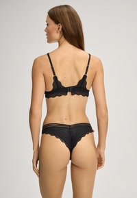 Schwarzes Spitzen-Bralette- und Tanga-Set mit filigranen Mustern, verstellbaren Trägern und gewellten Kanten. Weiches Material mit zartem Design.