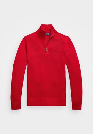 Pull en tricot rouge à manches longues, col demi-fermeture éclair et petit logo sombre sur la poitrine gauche, posé à plat sur un fond blanc.