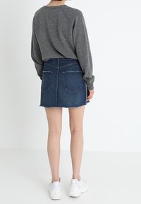 Top gris de manga larga, falda de mezclilla azul con dobladillo desflecado, vista trasera. Zapatillas blancas, líneas limpias, detalles mínimos.