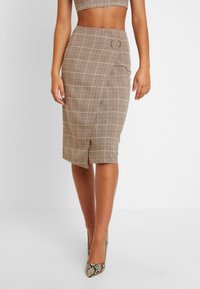 Jupe crayon à carreaux marron avec fente latérale, ornée d'un accent circulaire et d'une coupe ajustée. Fabriquée en tissu texturé avec des lignes horizontales et verticales.