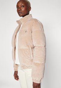 Giacca a vento rosa chiaro realizzata in un morbido tessuto opaco, con colletto alto, chiusura con zip e un discreto logo sul lato sinistro del petto.