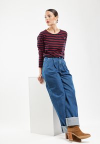 Stribet rød og marineblå langærmet skjorte parret med højtaljede, lysvaskede blå denimjeans. Tan ankelstøvler med stakhelt.