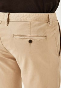 Khakifarbene Baumwollhosen mit einem nahtlosen Design, ausgestattet mit einer Knopftasche auf der Rückseite und dezenten Steppdetails in der Nähe des Bundes.