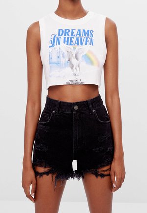Crop top blanc avec un graphisme bleu "DREAMS IN HEAVEN" mettant en scène une licorne et un arc-en-ciel, associé à un short en denim noir avec des bords effilochés.