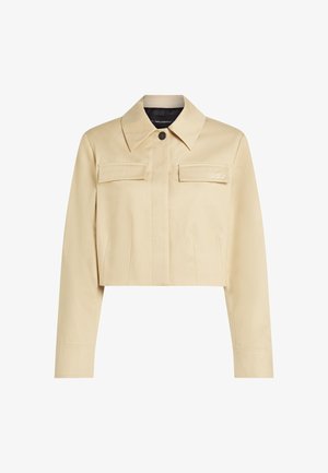 Beskåret beige jakke med spidse kraver, to frontlommer og knaplukning. Glat tekstur og diskret branding på brystet.
