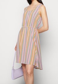 Vestido multicolorido con un diseño geométrico en rosa, azul y amarillo. Diseño sin mangas y cintura ajustada, combinado con un bolso en color lila.
