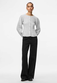 Gaiši pelēks adīts kardigāns ar garām pūkainām piedurknēm, aprīkots ar apaļu izgriezumu, pogu aizdari un nedaudz paplatinātu apakšmalu, apvienots ar melnām platām biksēm.