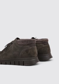 Chaussures en daim brun foncé avec un col en chevrons texturé, forme arrondie et semelle en caoutchouc flexible dotée de rainures pour une meilleure traction.