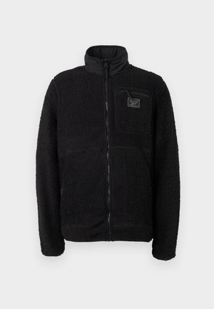 Svart zip-up fleecejakke med en teksturert, fluffy overflate, stående krage og en brystlomme med et merketikett.