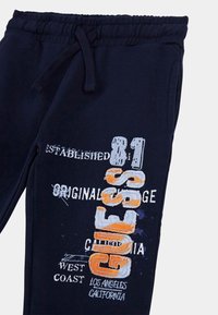 Pantalones de chándal azul marino hechos de una mezcla de algodón, con texto y gráficos bordados en blanco y naranja, cintura elástica con cordón.