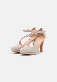 Beige suede high heels with a rounded toe, adjustable ankle strap, and a semi-platform design. Wooden heel adds height.