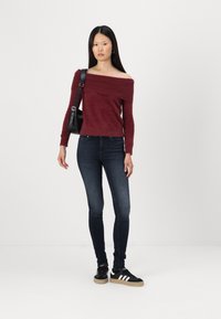 Pulover tricotat bordeaux cu umeri goi și mâneci lungi, asociat cu blugi negri skinny și adidași negri cu dungi albe.