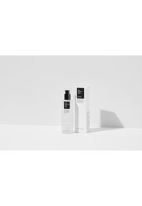 Bouteille en plastique transparent avec un bouchon-pompe noir, étiquetée "Liquide BHA contre les points noirs," à côté d'une boîte carrée blanche avec du texte noir et de petits accents.