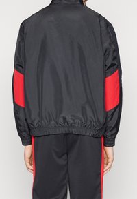 Svart satinjacka med röda paneler på ärmarna; elastisk nederkant och manschetter; enkel krage; ihop med matchande svarta träningsbyxor.