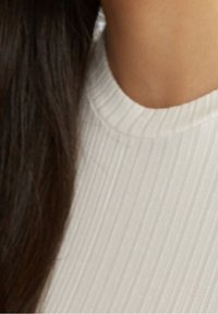 Mörkbrunt hår över vit ribbad tyg bredvid tan hud, med fokus på axel- och nackområdet.