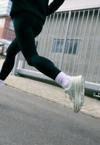 Leggings de corrida pretos combinados com meias brancas e ténis esportivos verde claro apresentam um design elegante e material flexível para movimento ativo.