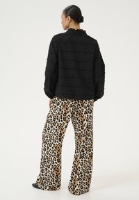 Blusa nera con texture e motivi ondulati, colletto con ruche, abbinata a pantaloni larghi a stampa leopardata nei toni beige e neri.