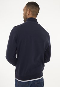Navy-blaues Zip-Hoodie mit hohem Kragen, gerippten Bündchen und Saum. Weicher Stoff, taillierte Passform und minimale Nähte auf der Rückseite.
