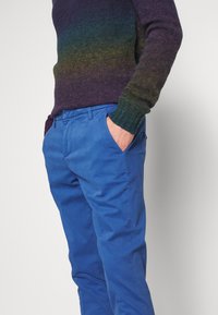 Neulepuuvilla purppuran ja vihreän gradienttivärin yhdistelmä, joka on yhdistetty sinisiin puuvillatrikoisiin housuihin. Neuleessa on pyöreä pääntie ja ribbireunat.