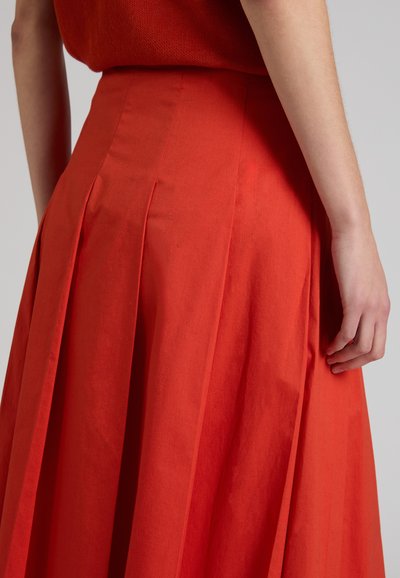 Mujer con falda roja plisada de talle alto y top rojo a juego, vista desde atrás con el brazo relajado a un lado.