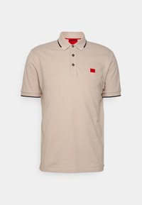 Polo beige avec des bordures noires, patte de boutonnage à trois boutons et écusson de marque rouge sur la poitrine. Tissu en coton doux avec des manches courtes.