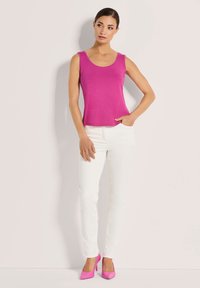Figurbetontes pinkes Tanktop mit Rundhalsausschnitt, kombiniert mit weißen Skinny Jeans. Das Modell trägt passende pinke High Heels. Glatte Textur und lässiges Design.