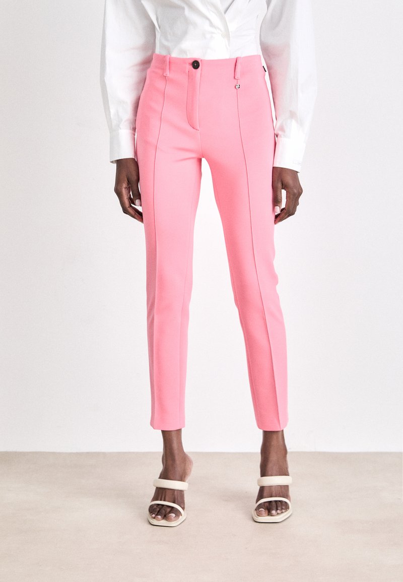 Pink tailored trousers with a slim fit, featuring vertical seams and front pockets. Paired with light-colored strappy sandals.