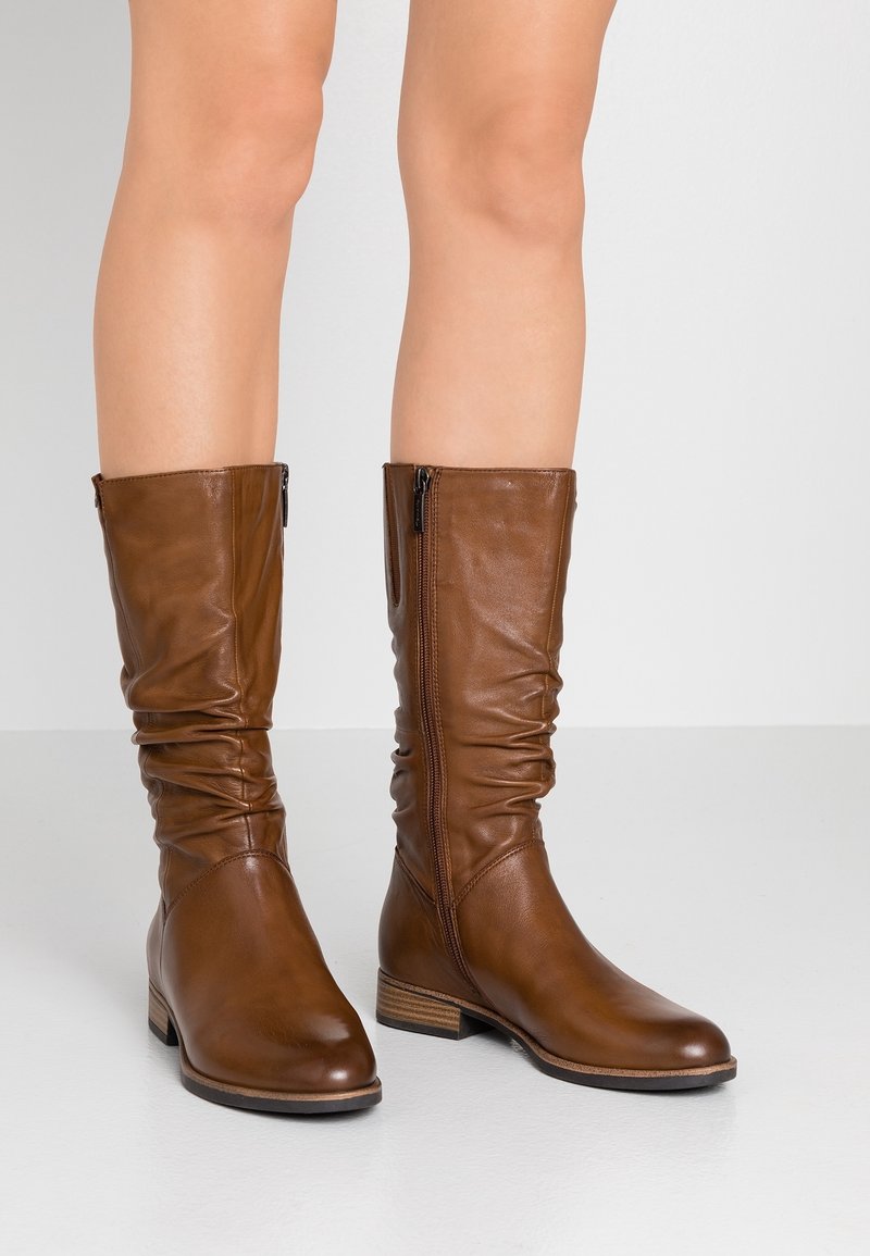  bottes montantes marron en cuir avec un design froissé, fermeture éclair sur le côté, et un talon bas empilé. Texture lisse, accents minimalistes.