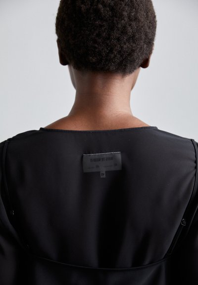 Indumento di colore nero con una texture liscia. Presenta un collo rotondo e un'etichetta di cura con la dicitura "MODI PER INDOSSARLO" sul retro.